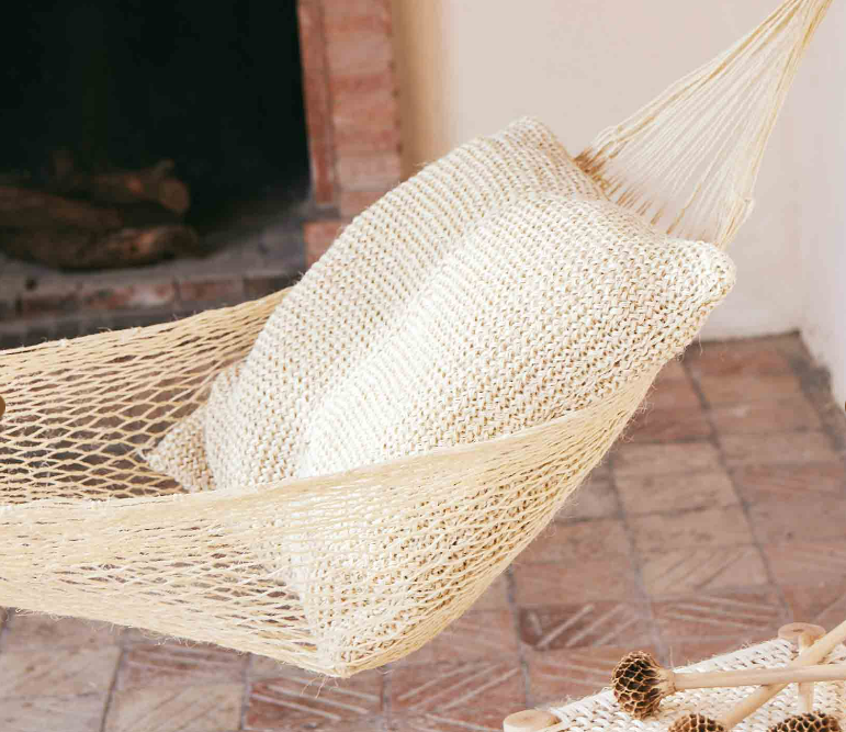 Beige hammock with a pillow made in natural fibre on a tiled floor.