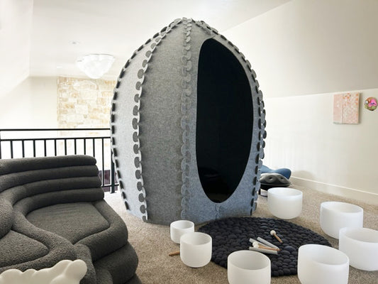 A free-standing pod designed with leaf-inspired tabs, made from recycled PET felt, sound absorbing, and lightweight. The pod is intended for up to 6 people and is shown in a room setting with various white elements around it.