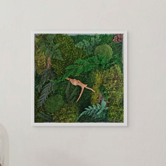 A framed artwork featuring a forest floor scene with moss, ferns, and a figure lying down, set against a white background.