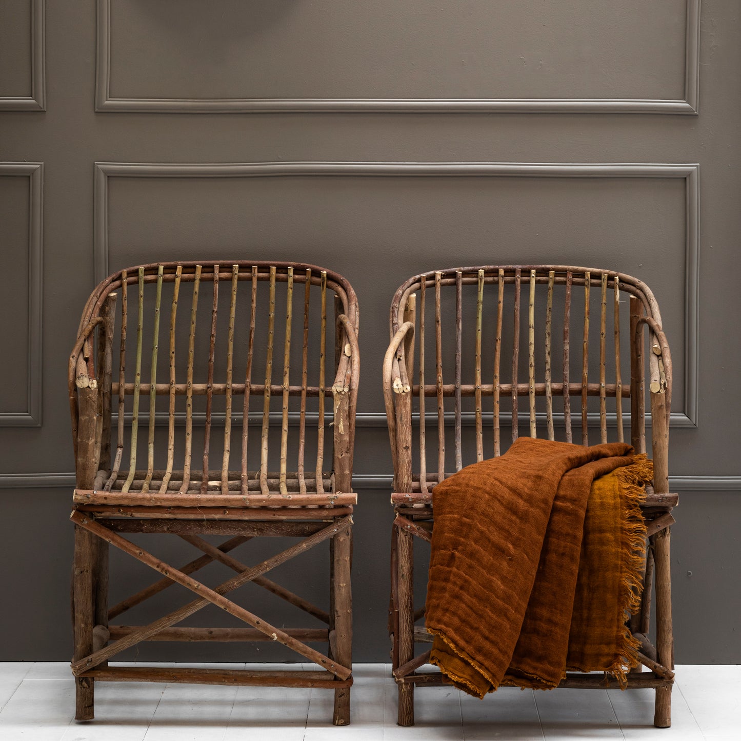 Two cabanna chairs made from oleandre chranches with linen folded cover  against a gray paneled wall.