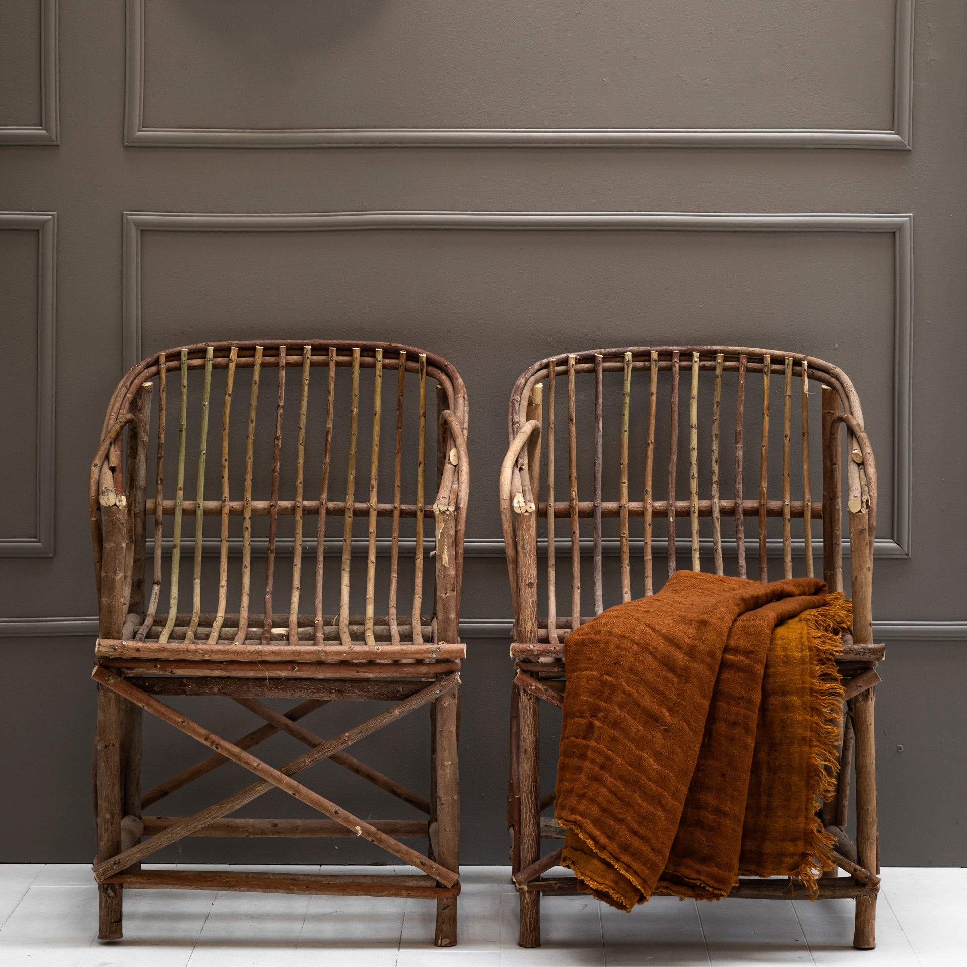 Two cabanna chairs made from oleandre chranches with linen folded cover  against a gray paneled wall.