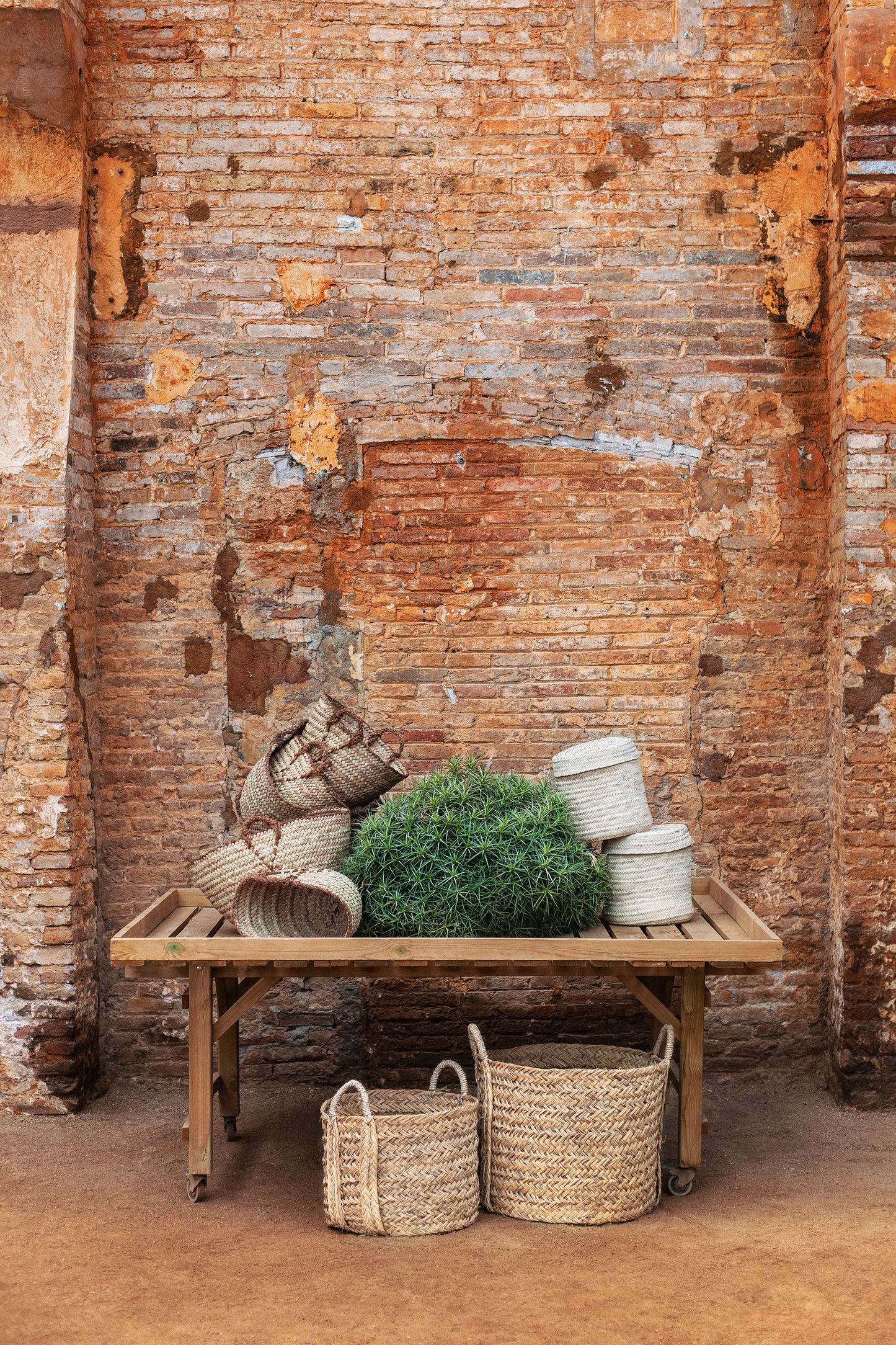 Wooden table with woven baskets  in natural material and plants against a rustic brick wall