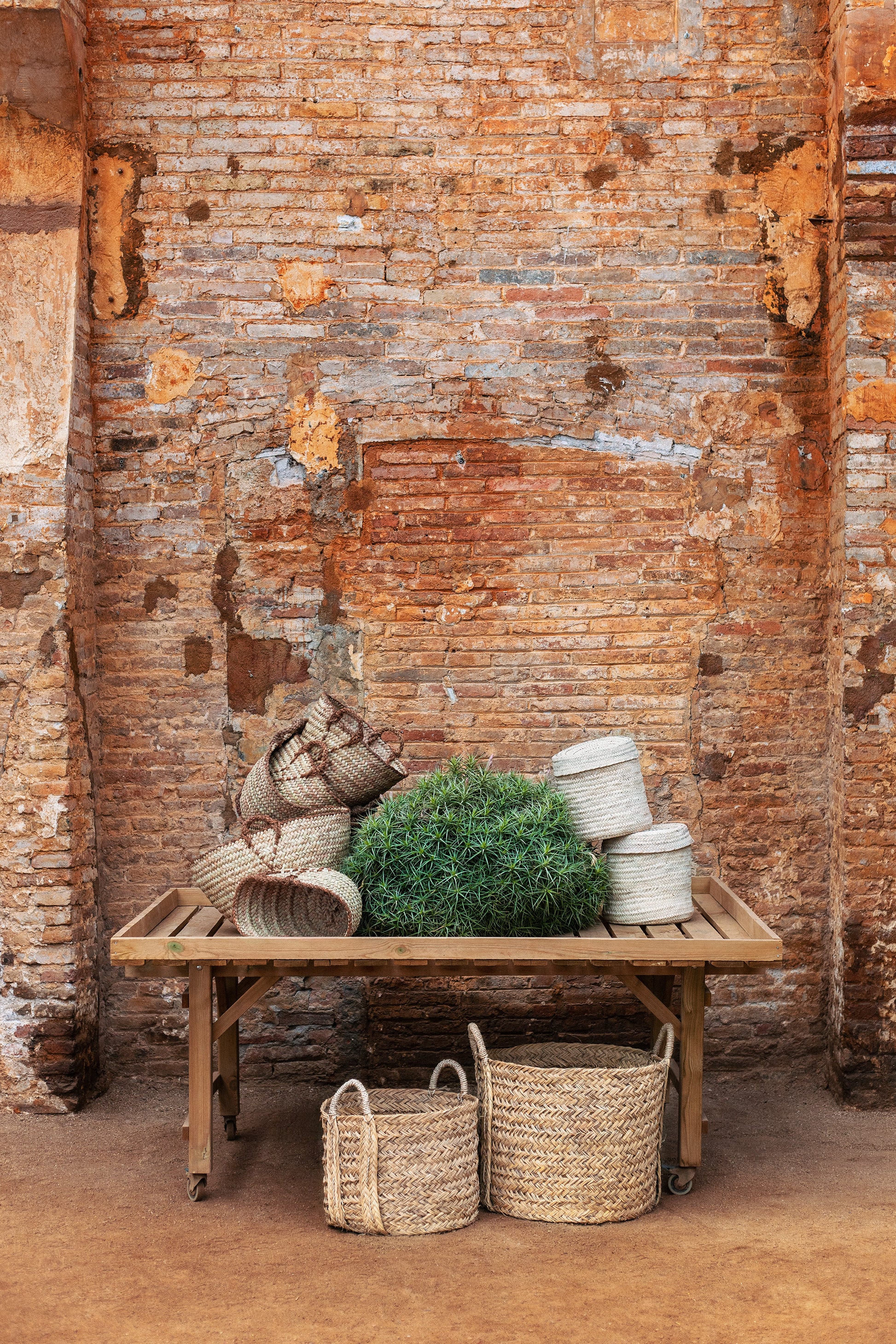 Wooden table with woven baskets  in natural material and plants against a rustic brick wall