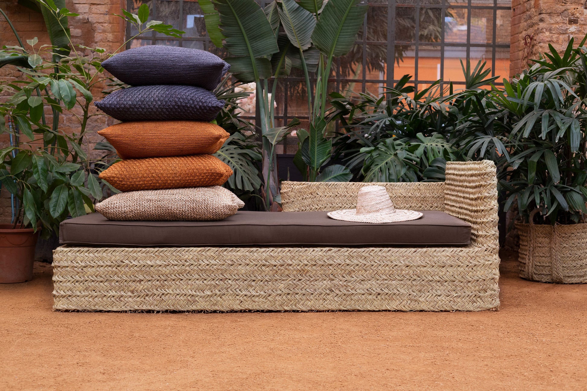 Daybed  with soft thin mattress and multiple cushions  and a hat on a patio with plants