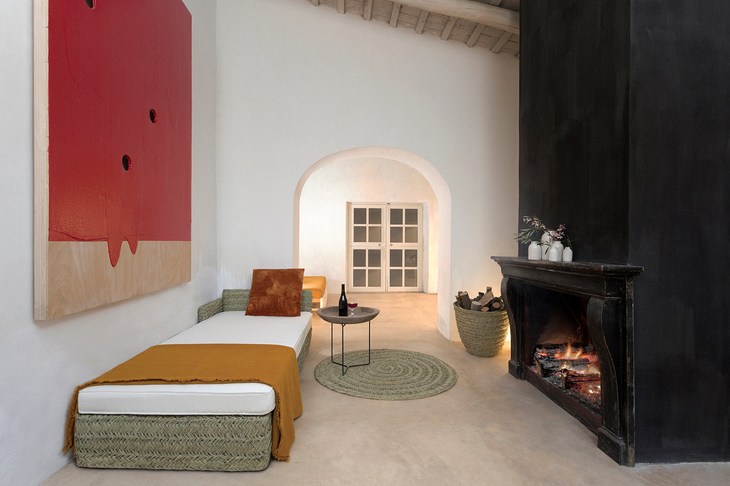 Living room with a fireplace, daybed made in natural fibres with thin white mattress brown plaid and cusion , and abstract art on the wall.