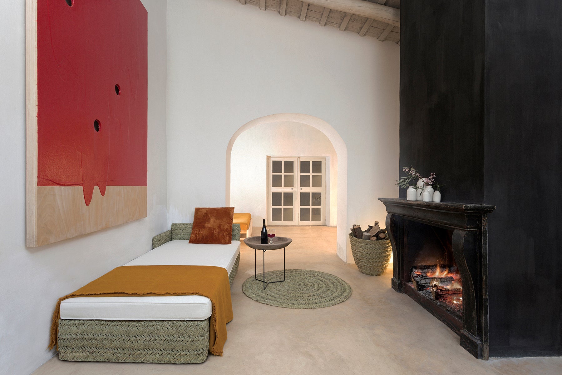 Living room with a fireplace, daybed made in natural fibres with thin white mattress brown plaid and cusion , and abstract art on the wall.