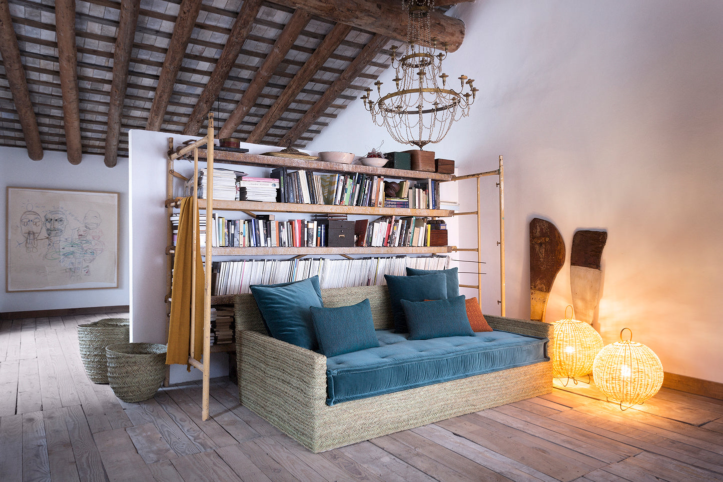 Cozy living room with a sofa made from natural fibre, esparto, with sea blue seating matress and cushions. behind it a bookshelf, and decorative lamps.